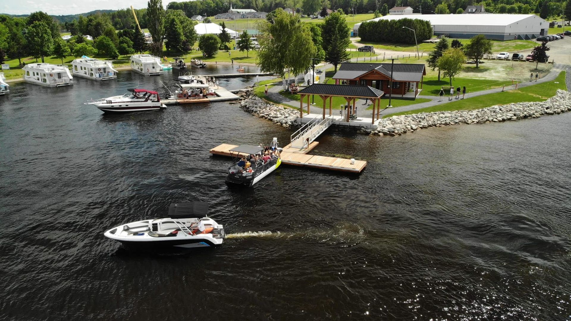Boats near a dock and gazebo on a lake, with buildings and trees in the background.