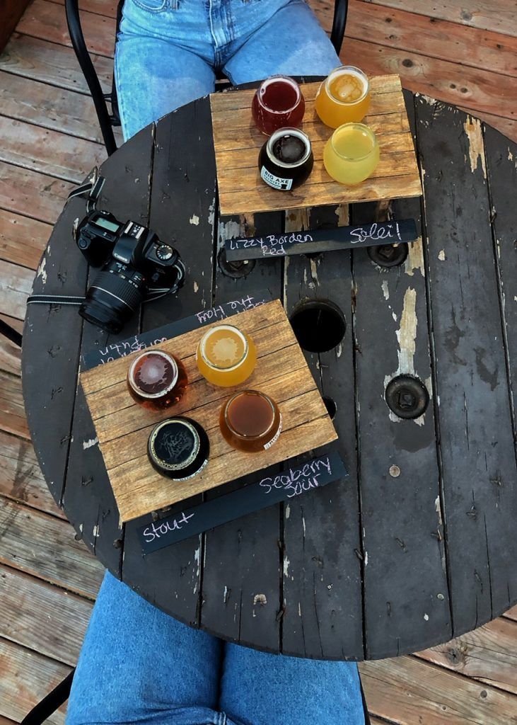 Two beer flights on a wooden table, with camera and person in jeans.