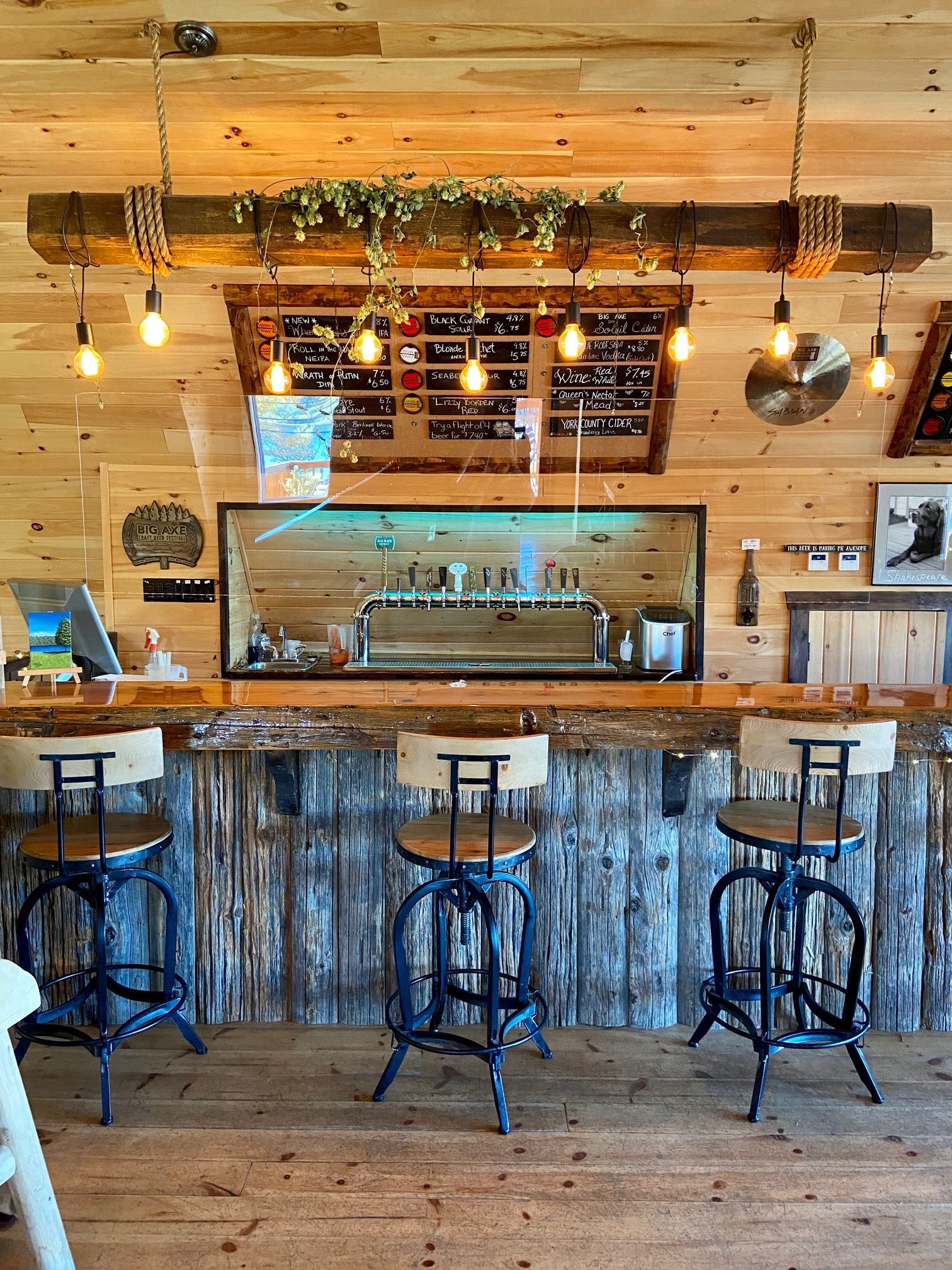 Rustic bar with wooden walls and ceiling, bar stools, and a tap system.