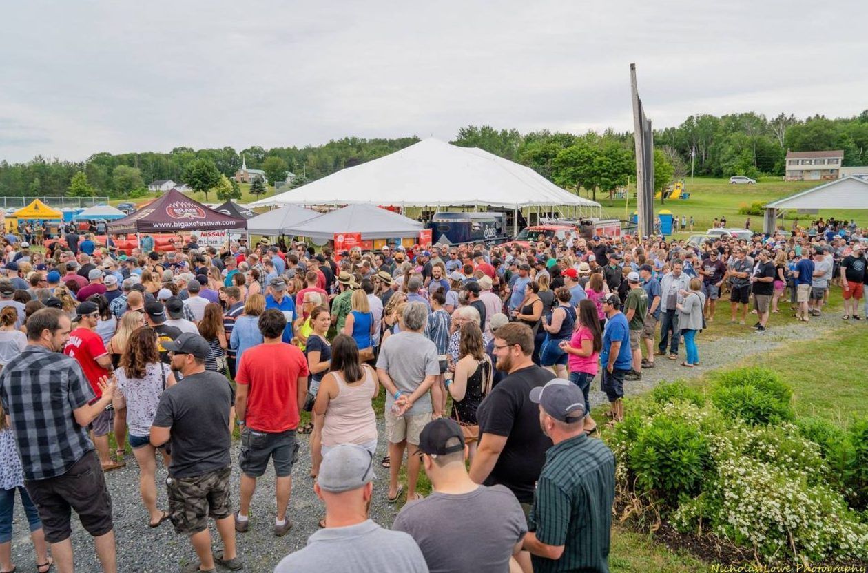 Large outdoor event with crowd gathered near tents and stage. Overcast sky.