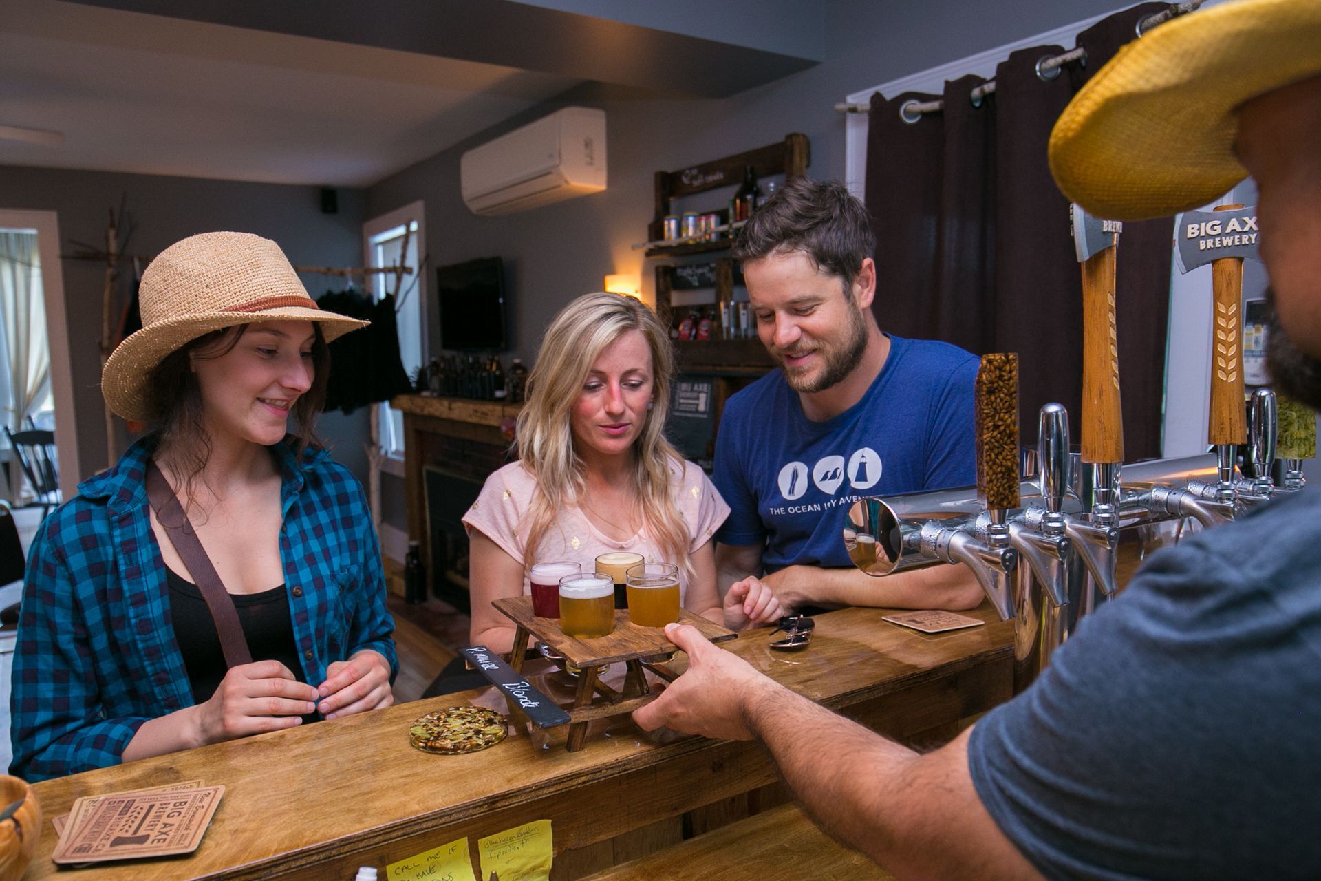 Patron receives beer flight at bar. Three people smiling; bar setting.
