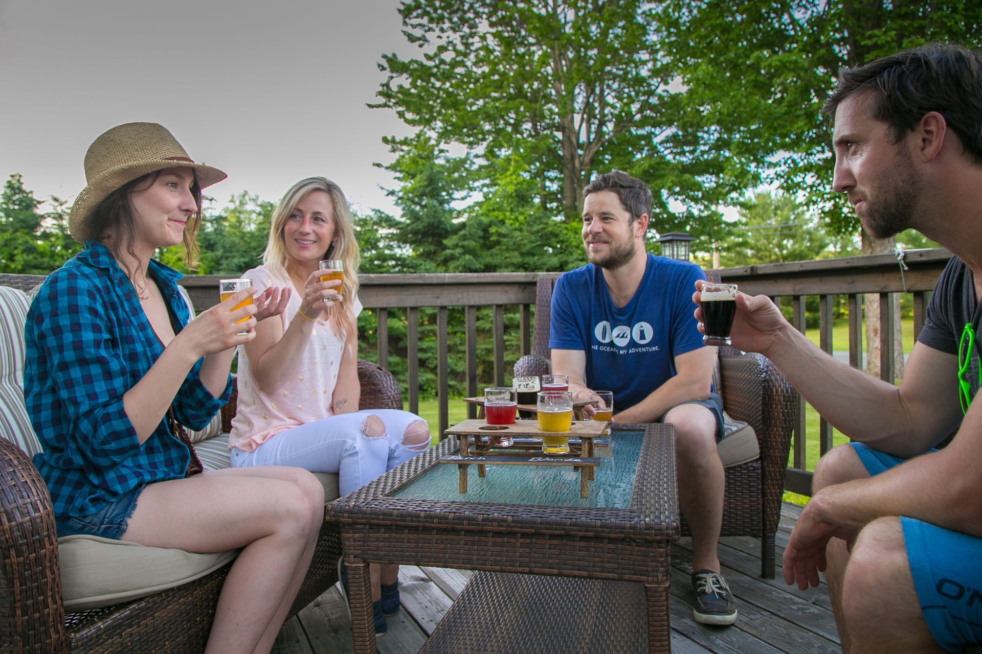 Four people toasting beer glasses on a wooden deck; a sunny day setting.