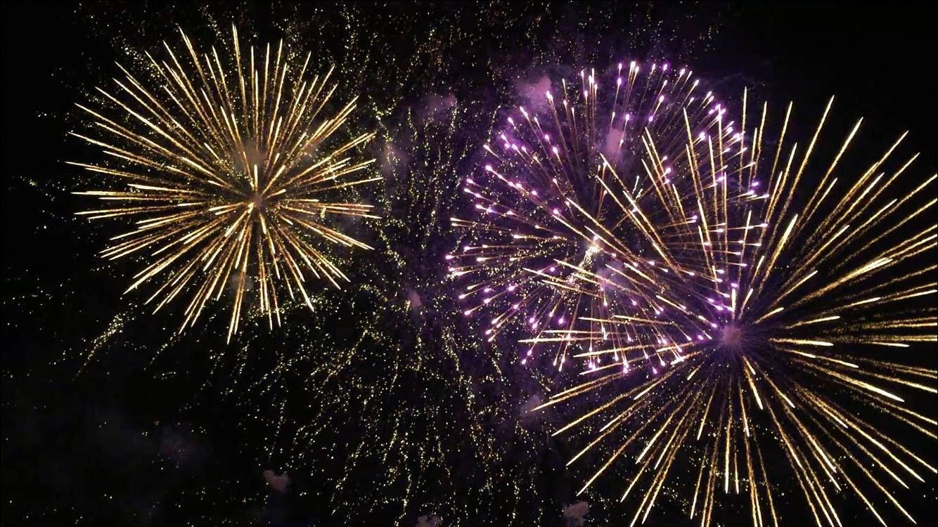 Golden and purple fireworks burst in the night sky.