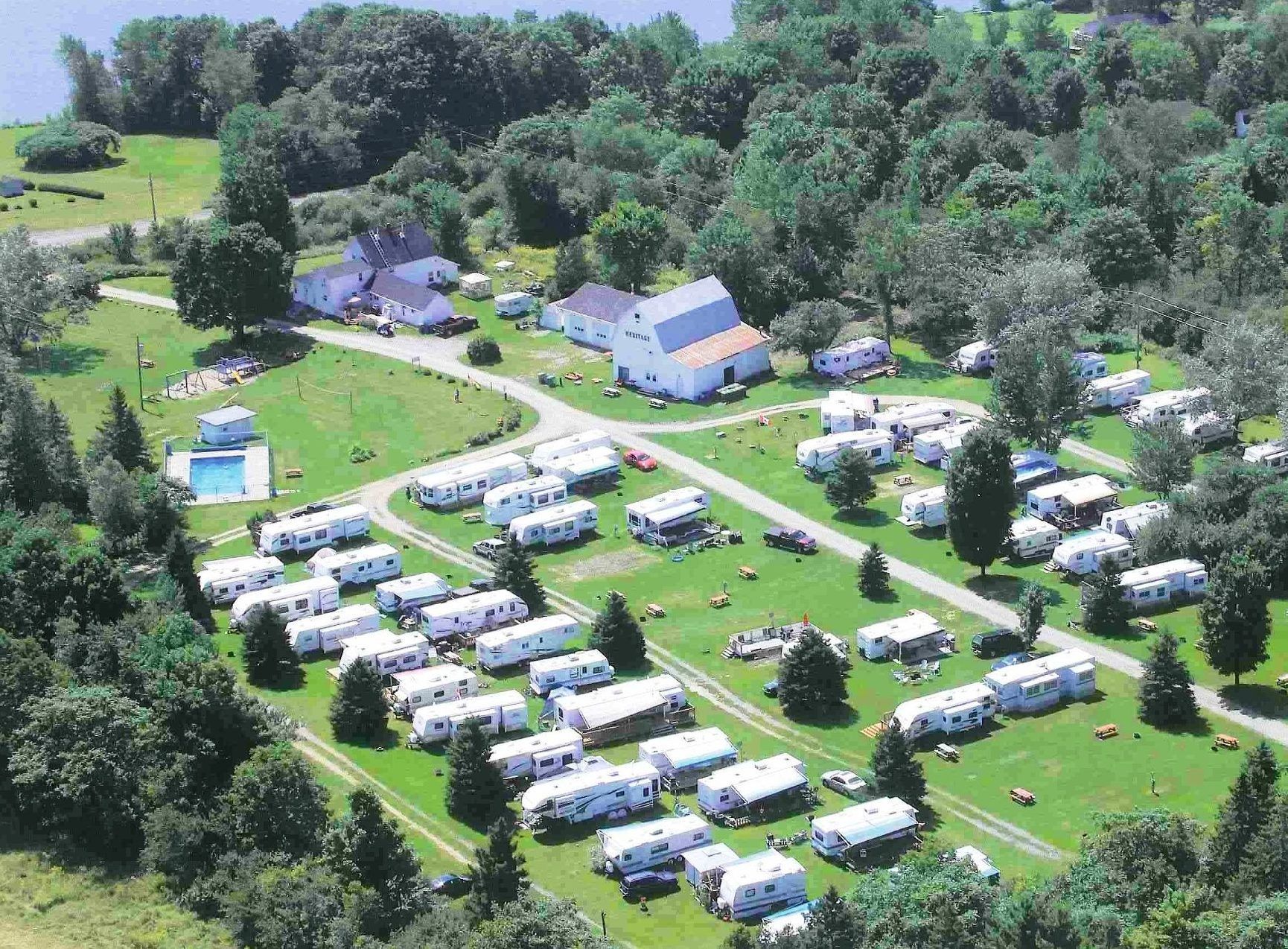 Aerial view of a campground with RVs, green grass, trees, and buildings near a body of water.