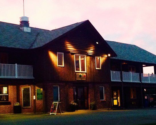 Two-story building with dark wooden siding, white balconies, and outdoor lighting at dusk.