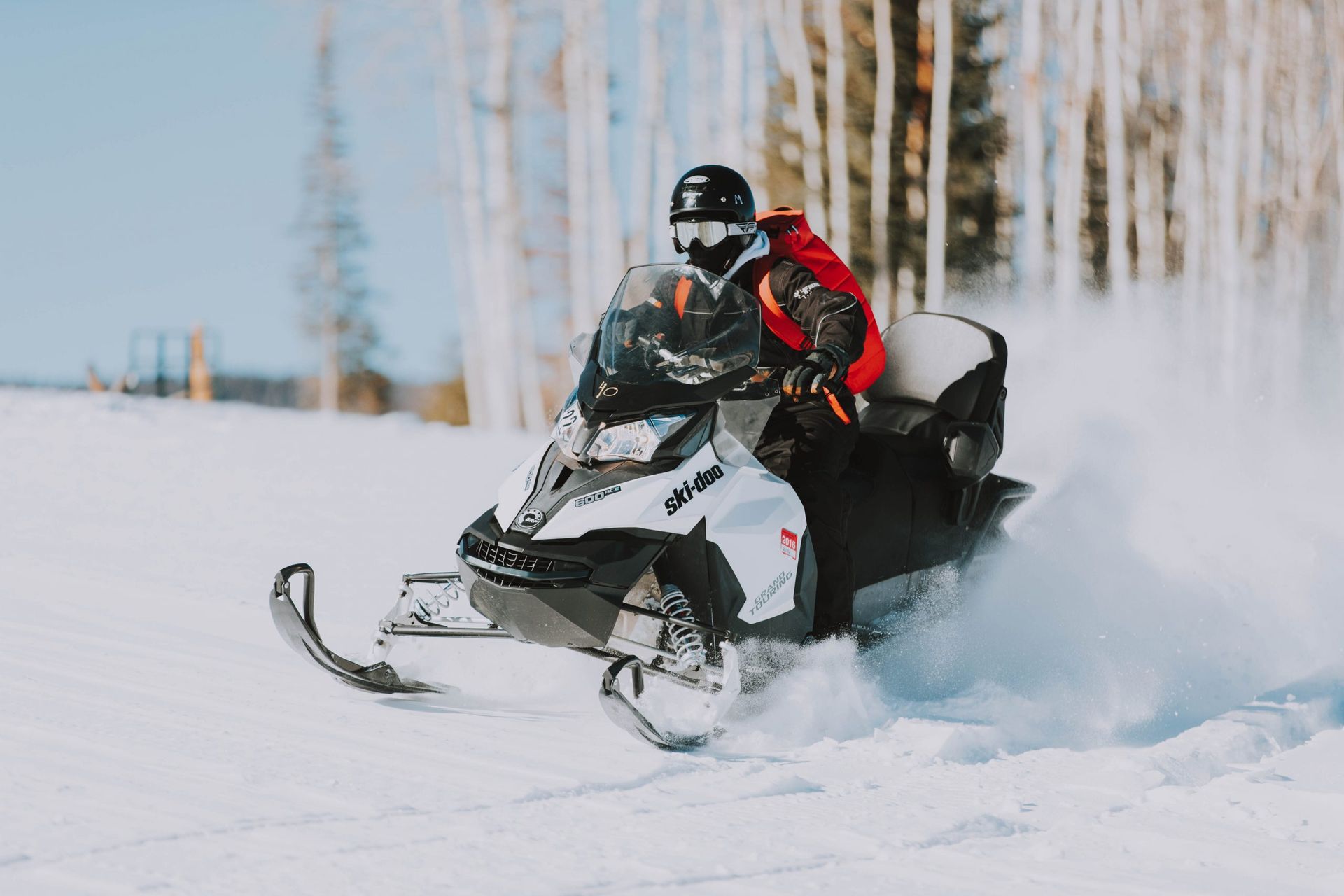 Snowmobiler on a white snowmobile kicks up snow. Blue sky, snow-covered landscape.