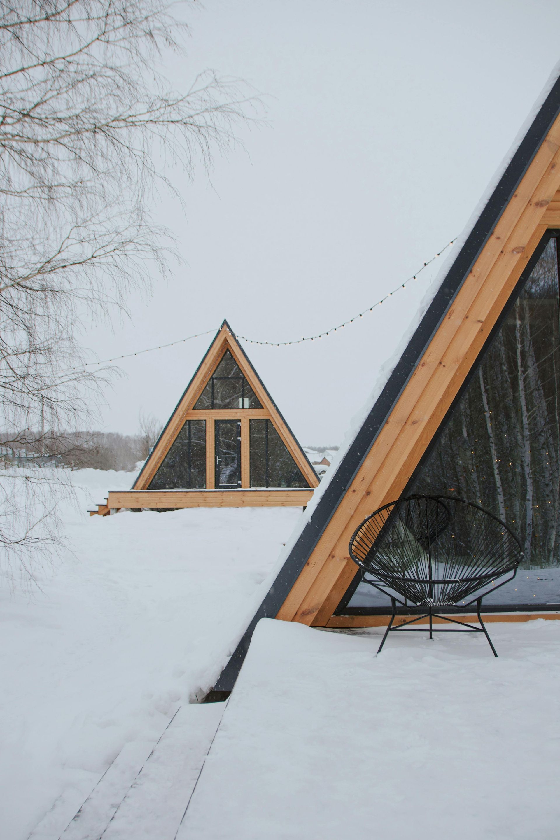 Snowy A-frame cabins, a black chair on a deck. Winter scene.