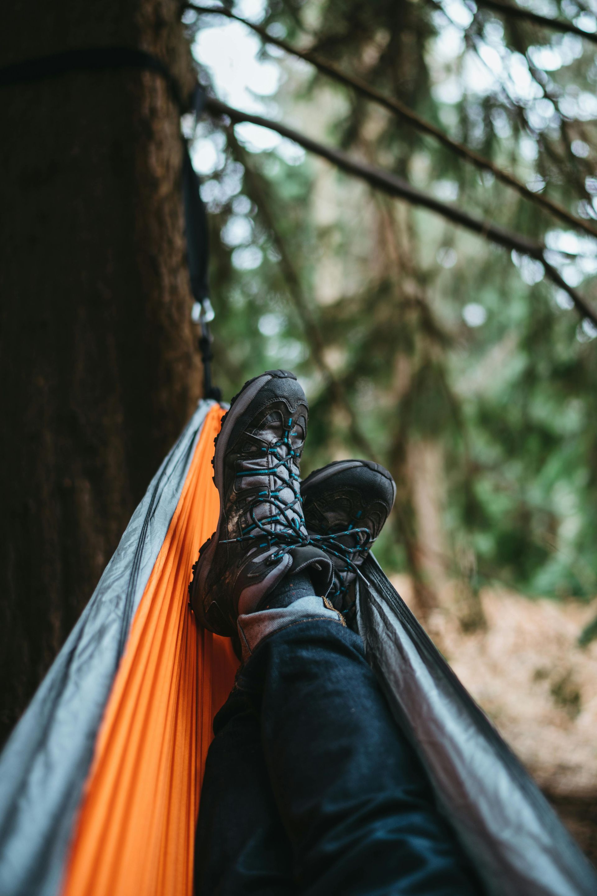 Person relaxing in a hammock in a forest; hiking boots visible.