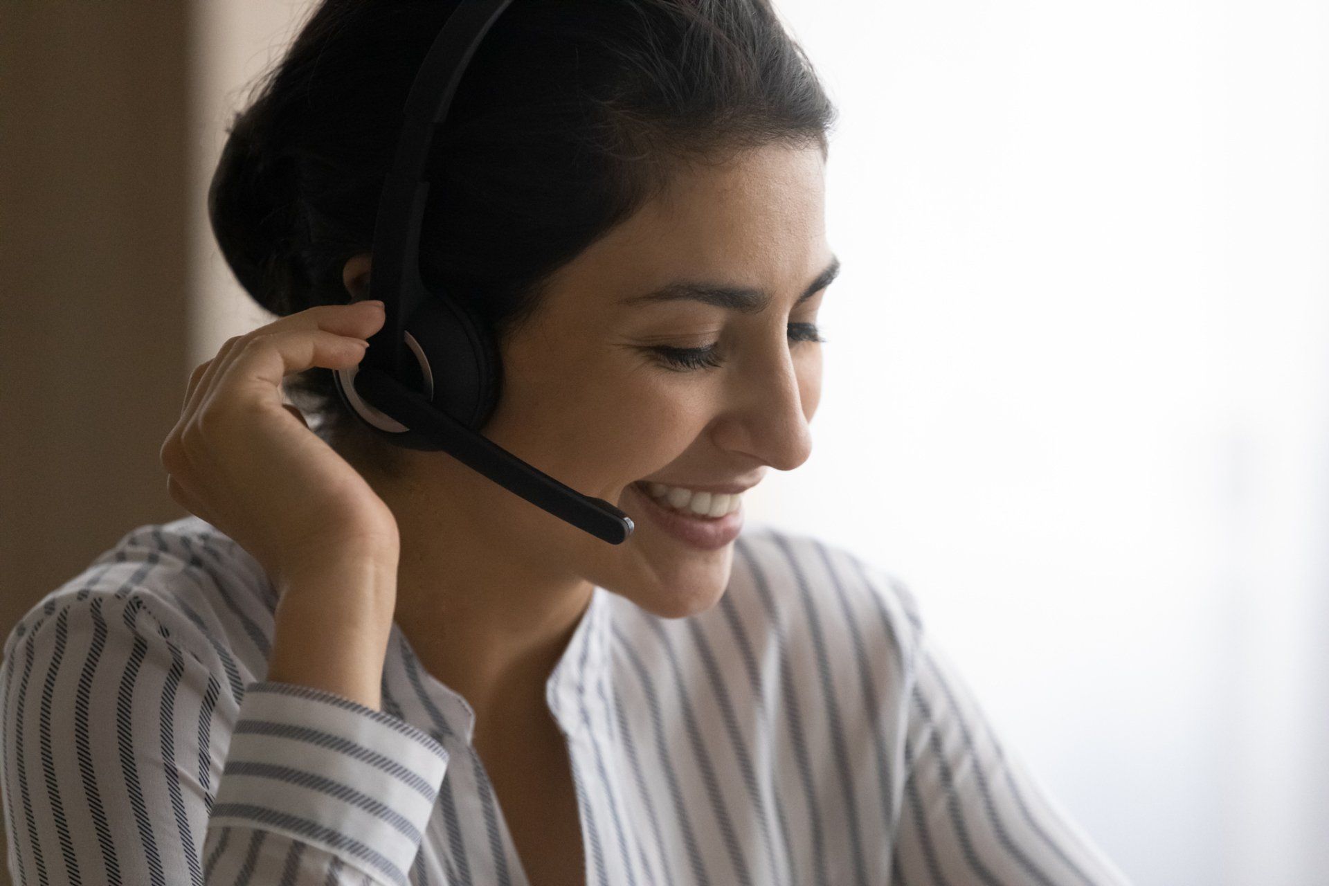 A woman wearing a headset is smiling while talking on a phone.