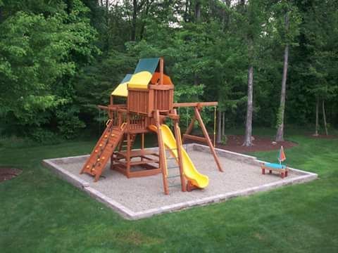 Wooden playground with a yellow slide and swing set in a yard with trees.