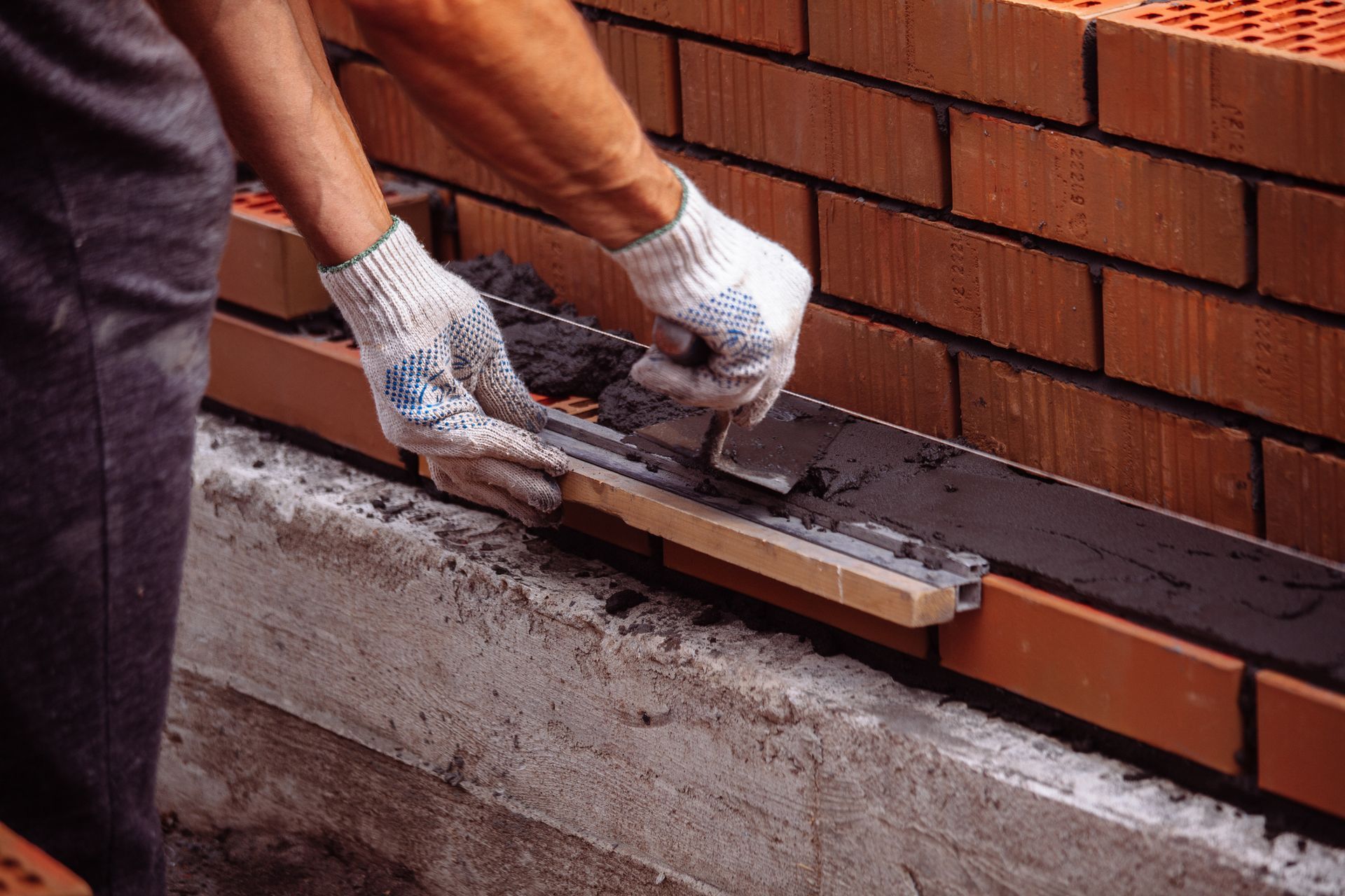 Worker laying bricks with mortar on a construction site.
