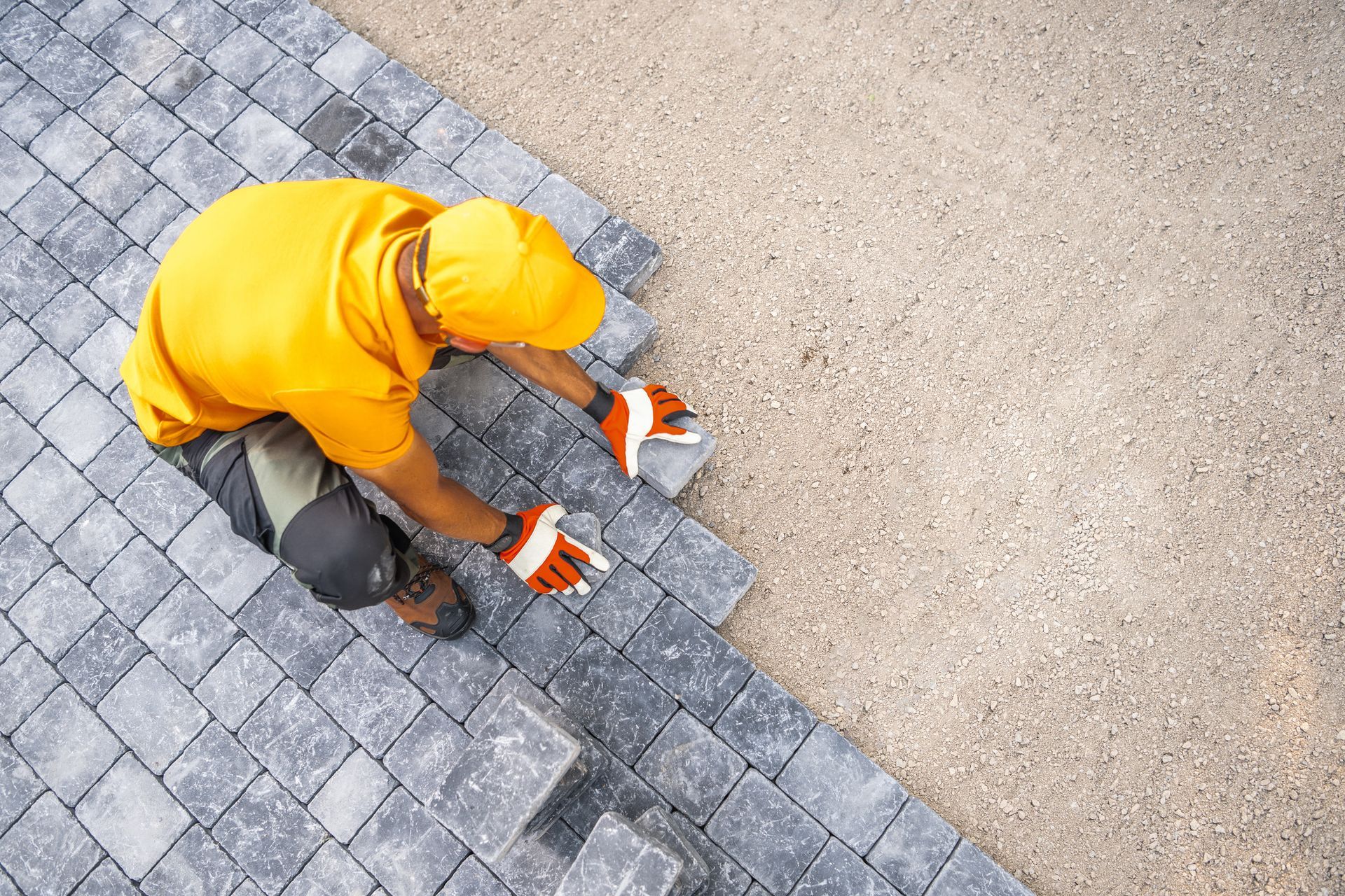 A hardscape design contractor in a yellow uniform is laying paving stones on a path
