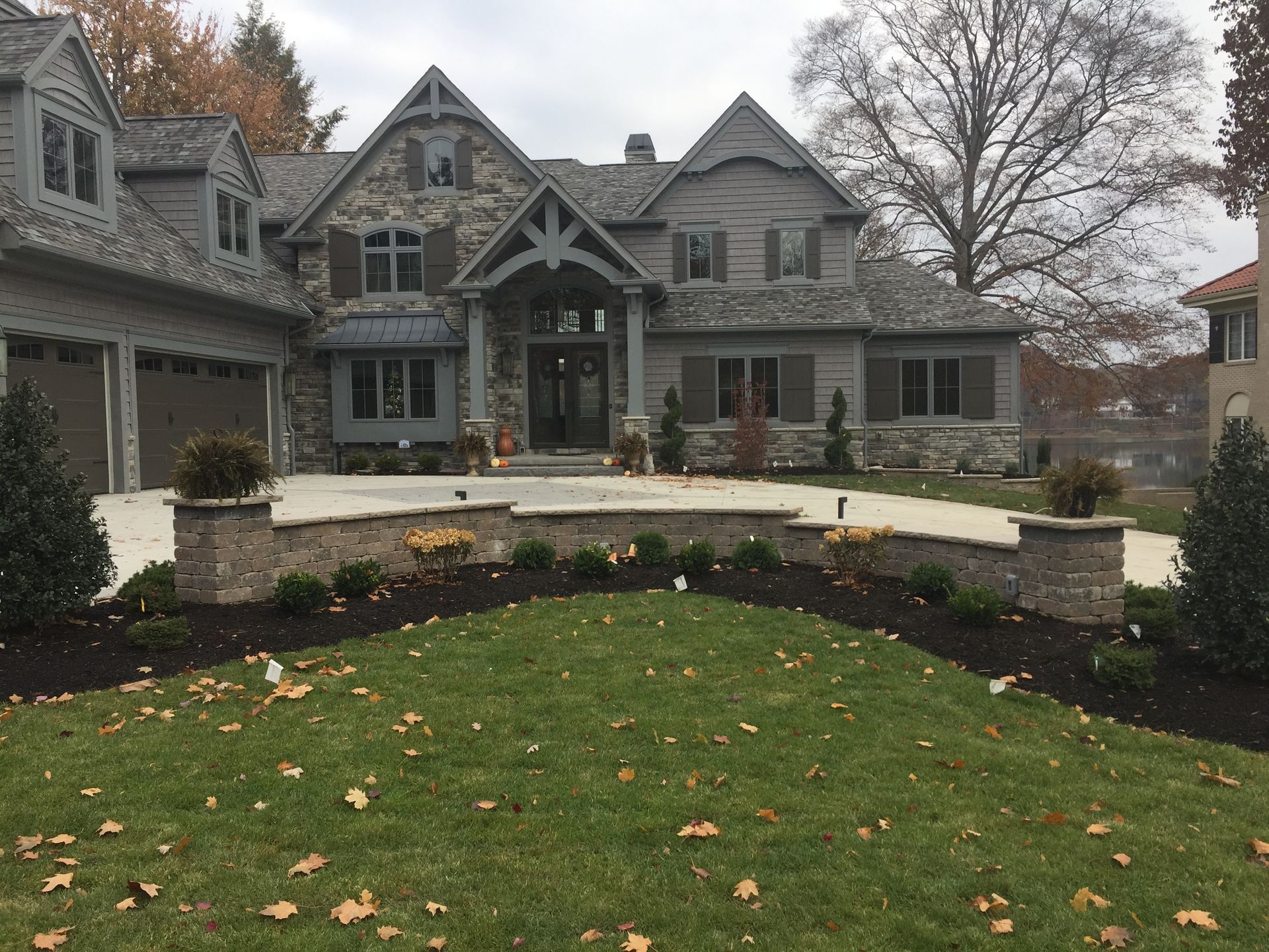 Stone-and-wood house with a landscaped lawn and driveway. Autumn leaves on the grass.