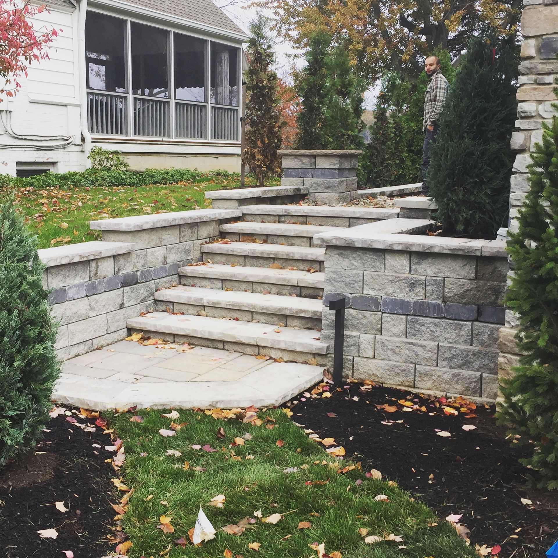 Stone steps and retaining walls in a landscaped yard, leading up to a house with a screened porch.