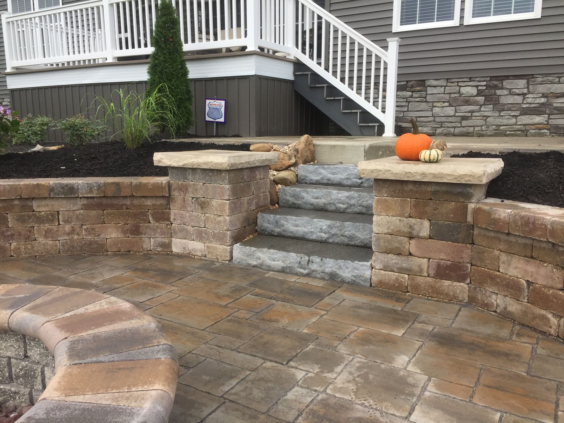 Stone patio with steps leading up to a house entrance, pumpkins on pillars, brown and tan brickwork.