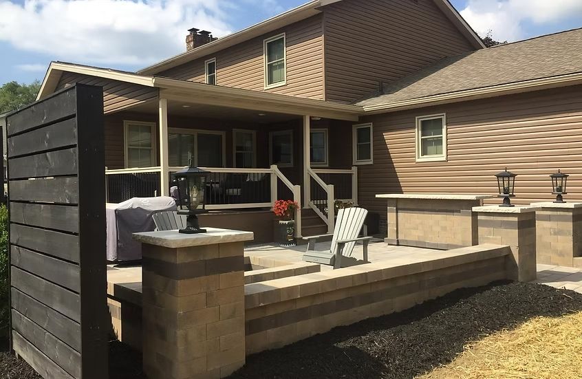 Patio with stone retaining walls, a wooden privacy screen, and a two-story house with a porch.