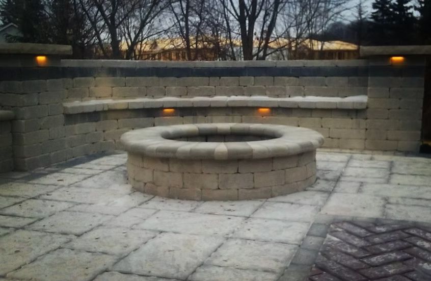 Stone patio with a fire pit, surrounded by a low wall with built-in lights.