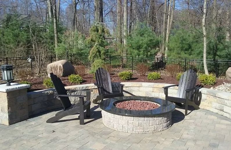 Patio with fire pit, Adirondack chairs, and surrounding retaining wall in a wooded area.