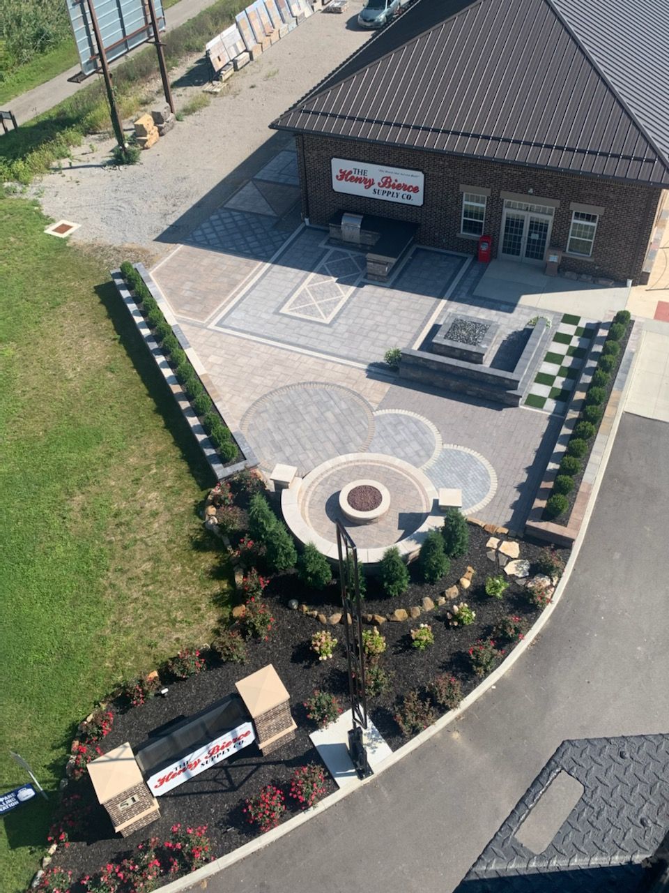 Aerial view of a brick building with a landscaped patio featuring pavers, a fire pit, and flower beds.