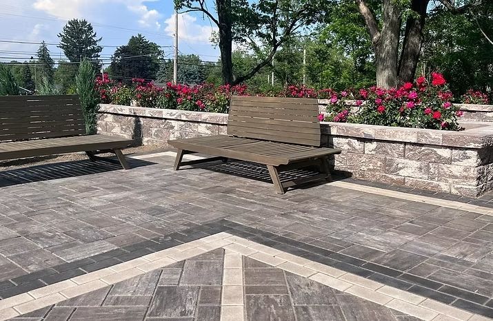 Two brown benches on a brick patio with a flower bed in the background.