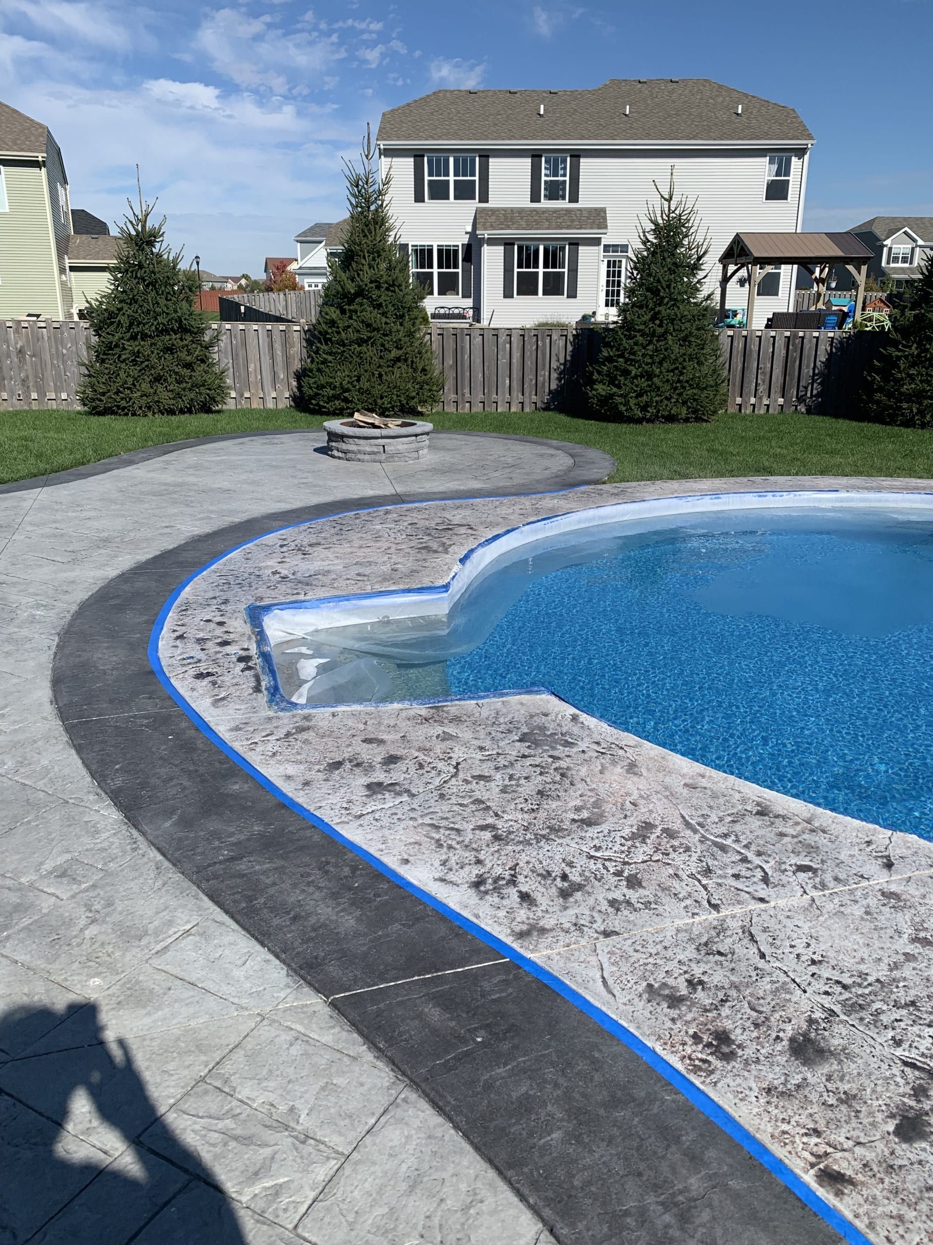 Backyard pool with blue water, curved stone deck, and a house in the background