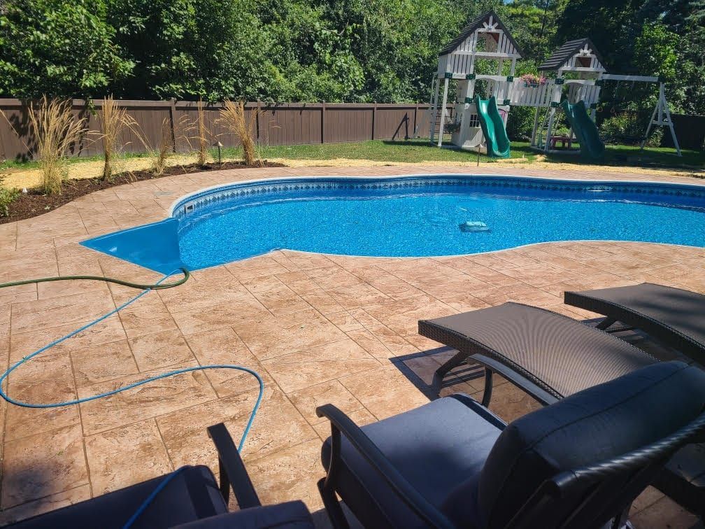 Backyard pool with tan patio, lounge chairs, garden hose, and playset in the background