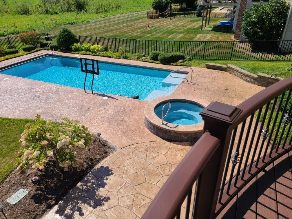 Backyard pool and hot tub with tan deck, black railing, and green lawn beyond