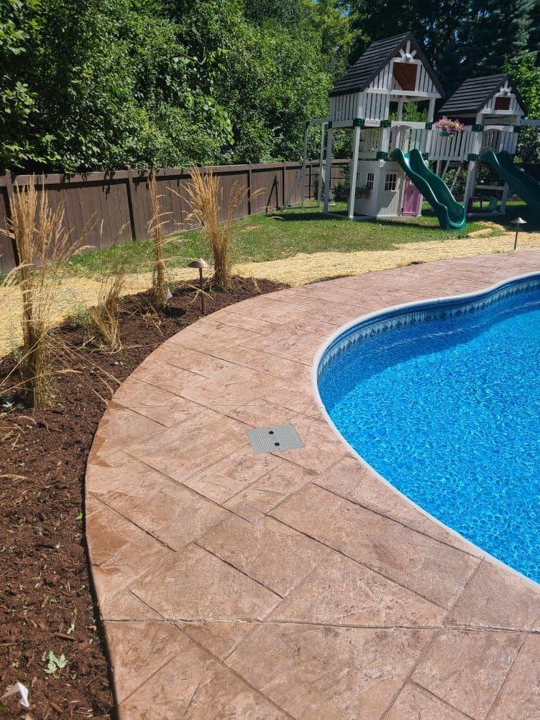 Backyard pool with stamped concrete deck, landscaped border, and children’s playset beside a wooden fence