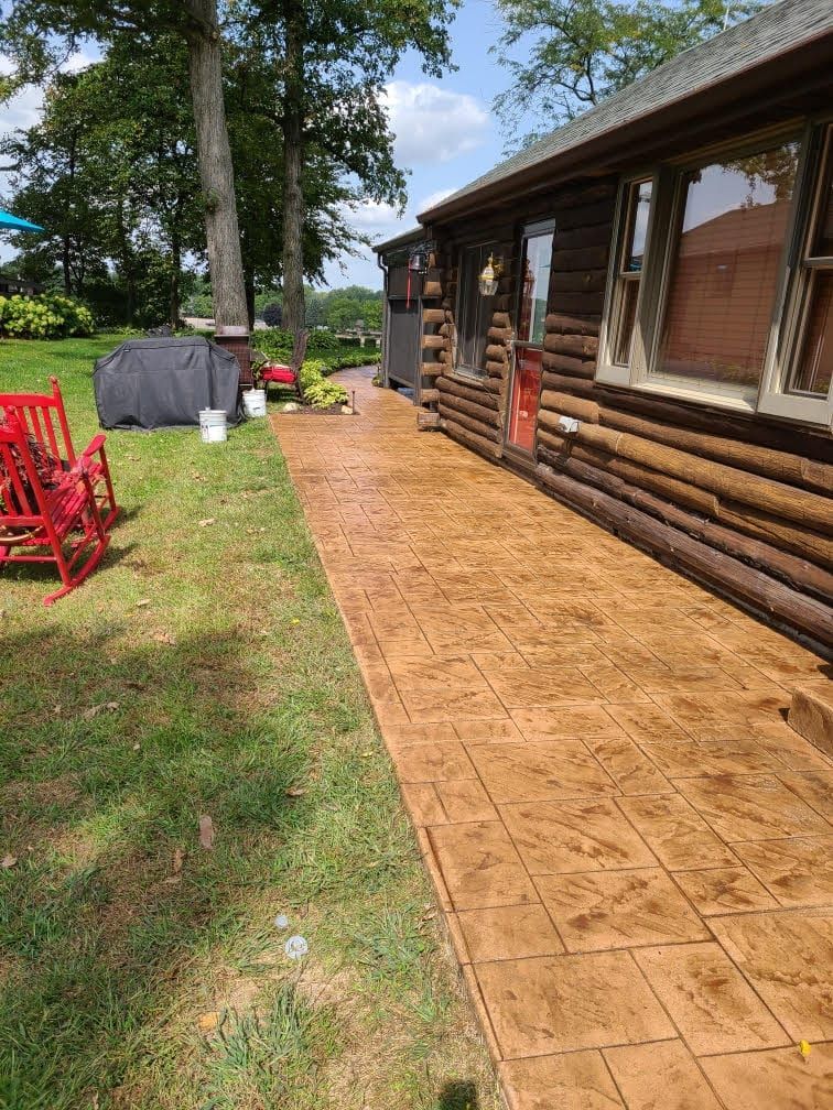 Freshly stamped concrete walkway beside a log cabin with red chairs and trees in a sunny yard