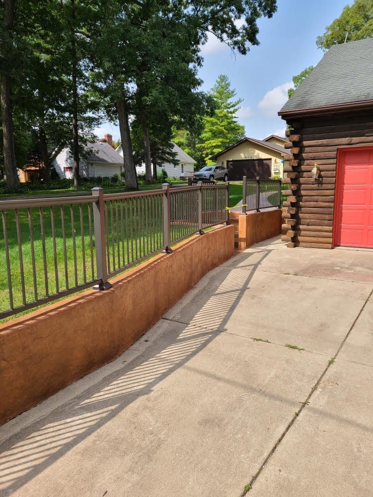 Concrete driveway beside a fenced yard and log garage on a sunny day