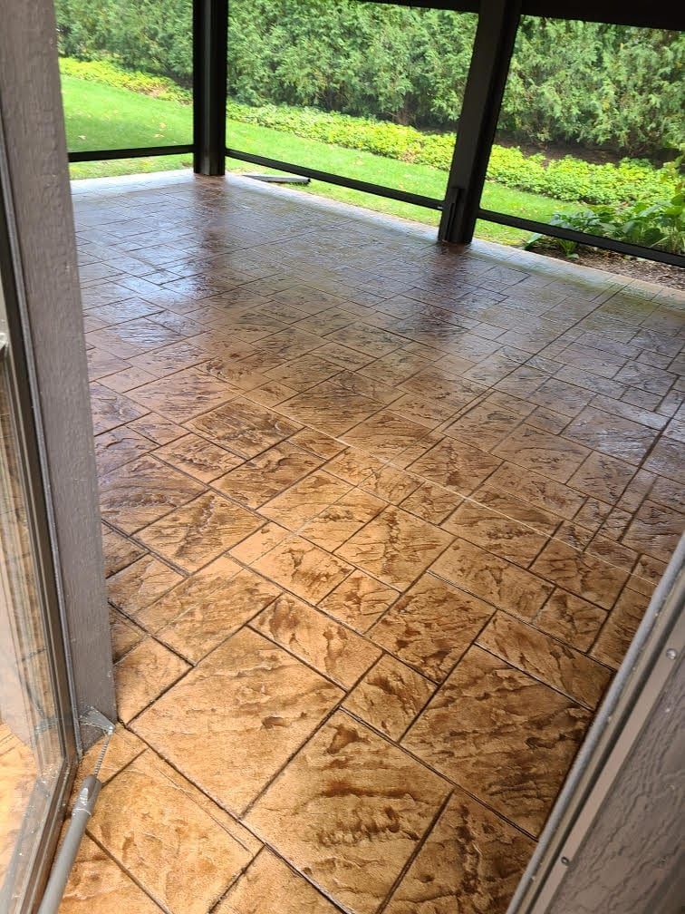 Wet stamped-concrete patio with screened porch posts and a green grassy yard beyond
