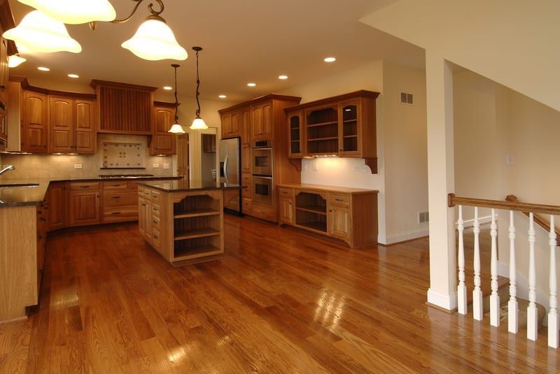Open kitchen and dining area with hardwood floors, wood cabinets, island, and hanging pendant lights.