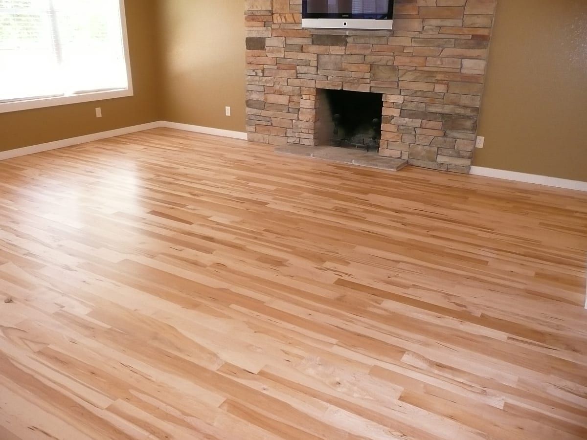 Empty living room with hardwood floors, tan walls, and a stone fireplace