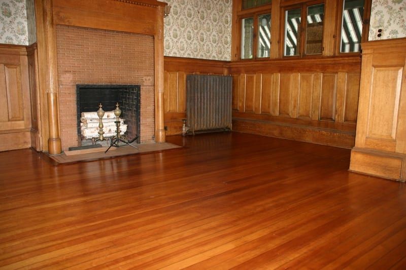 Empty wood-paneled room with a fireplace, radiator, and polished hardwood floor