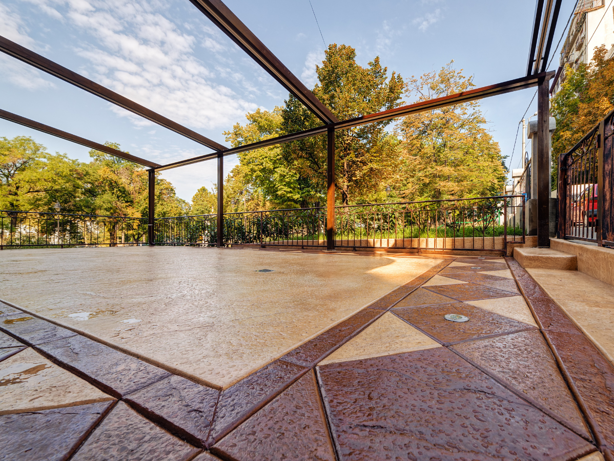 Empty stone patio with metal pergola framing trees and autumn foliage in a park