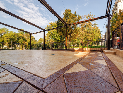 Empty stone patio with metal pergola framing trees and autumn foliage in a park