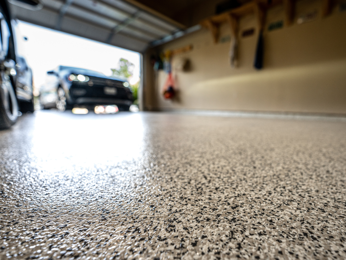 Low-angle view of a black car in an open garage with a speckled concrete floor