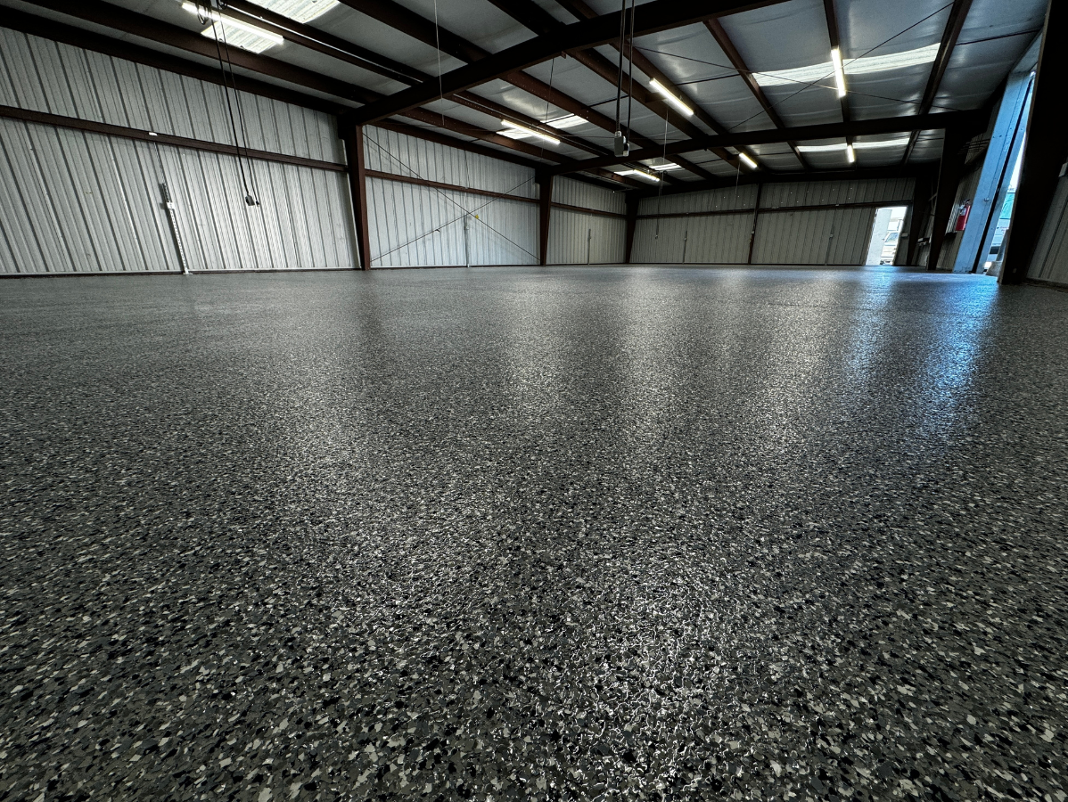 Empty industrial warehouse with a speckled epoxy floor and steel beams overhead