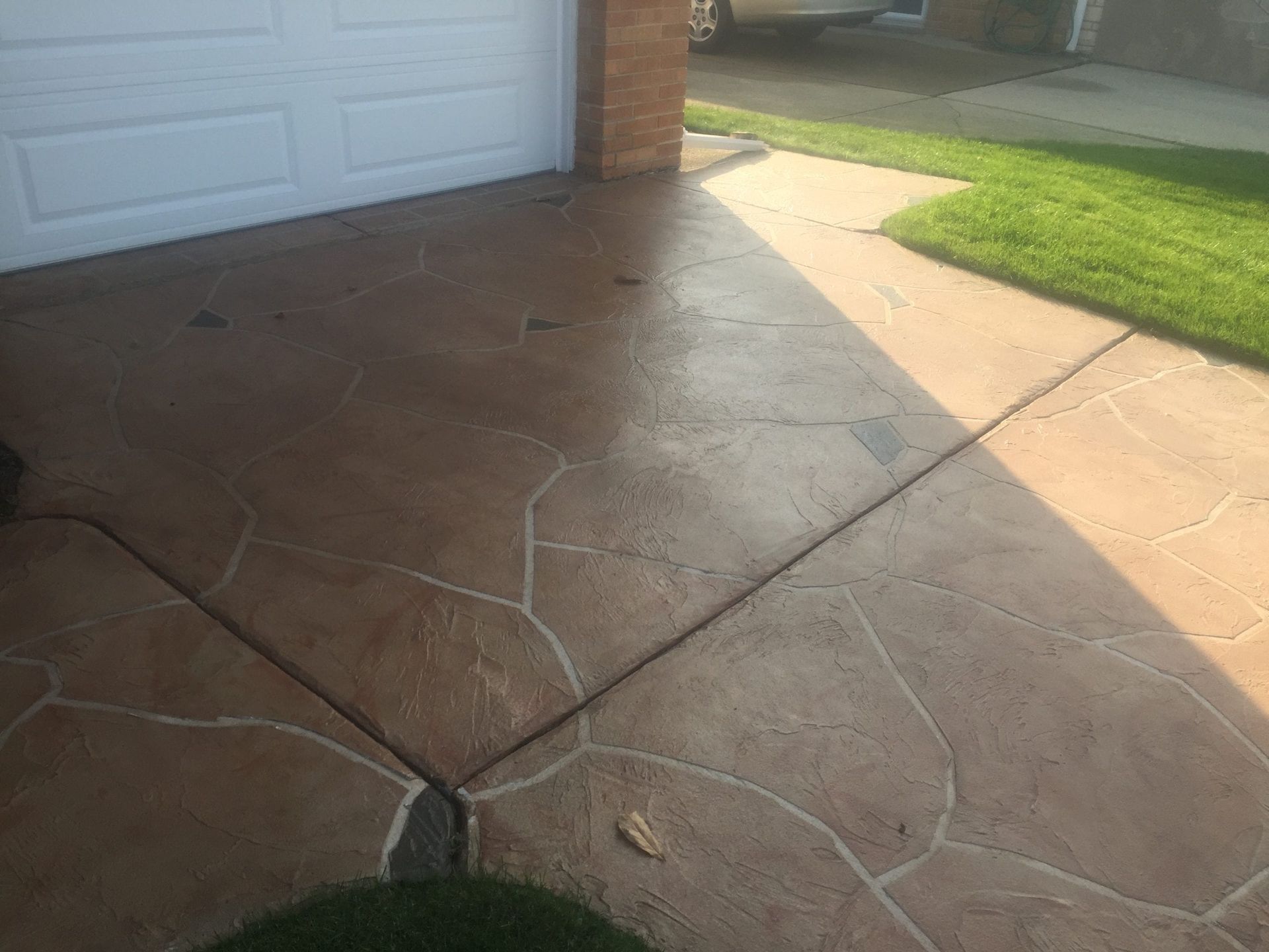 Stamped concrete driveway beside a garage, with sunlight and shadows across the walkway.
