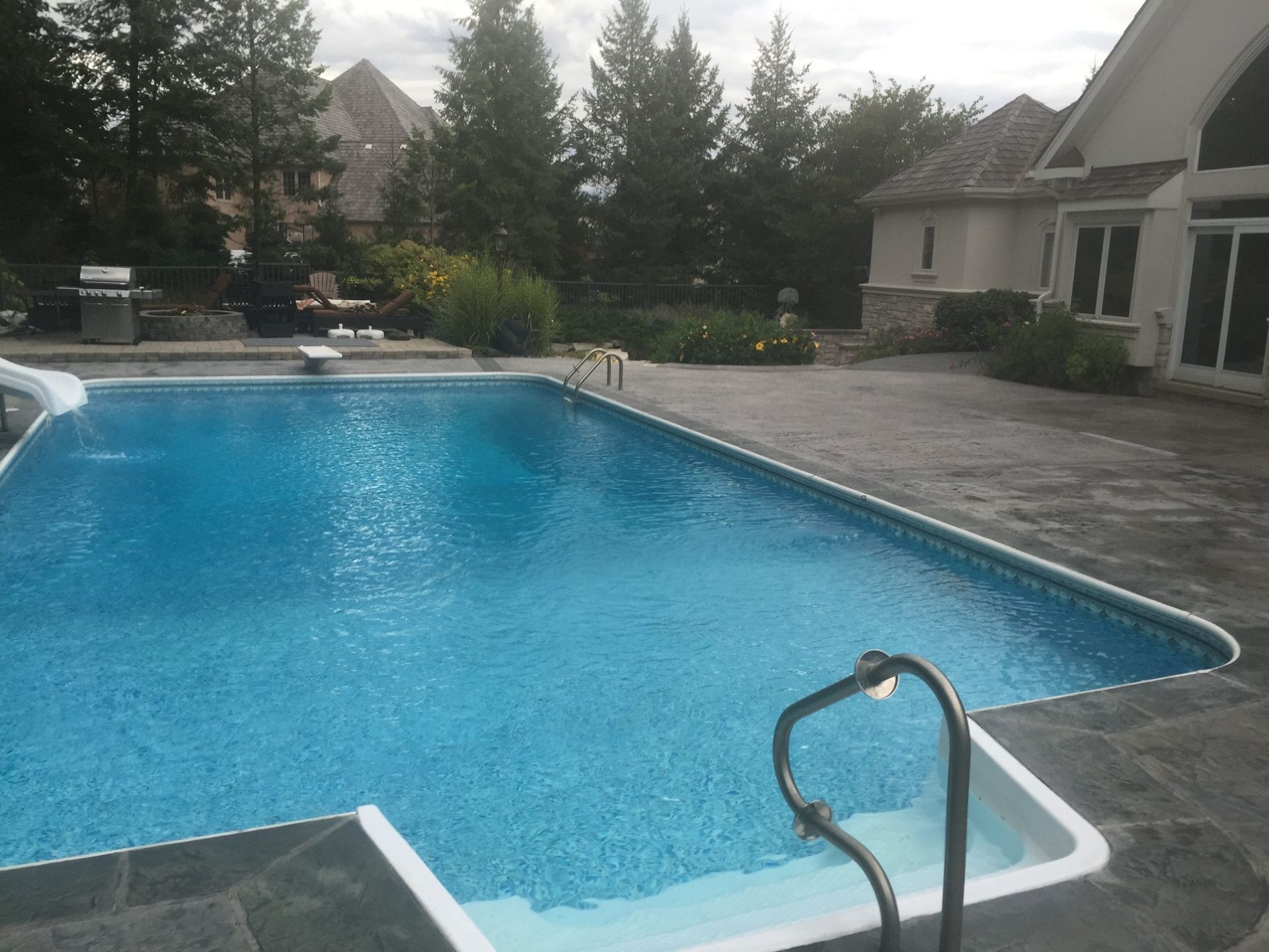 Outdoor swimming pool with blue water, concrete deck, and houses and trees in the background