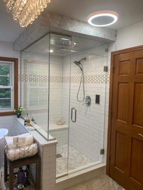 Walk-in shower with glass enclosure, white tile, rain showerhead, and wooden bathroom door.