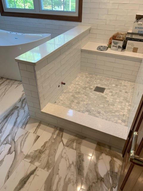 Tiled walk-in shower with built-in bench, marble-pattern floor, and window light in a bathroom