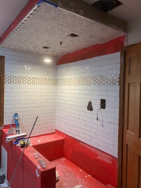 Partially renovated bathroom with red paint, white tile walls, and exposed plumbing under a tiled ceiling