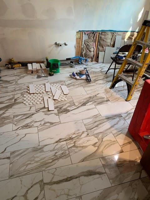 Partially tiled room with marble-pattern floor, tools, ladder, and renovation materials scattered around