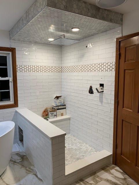 White tiled bathroom with a walk-in shower, glass partition, and wooden door