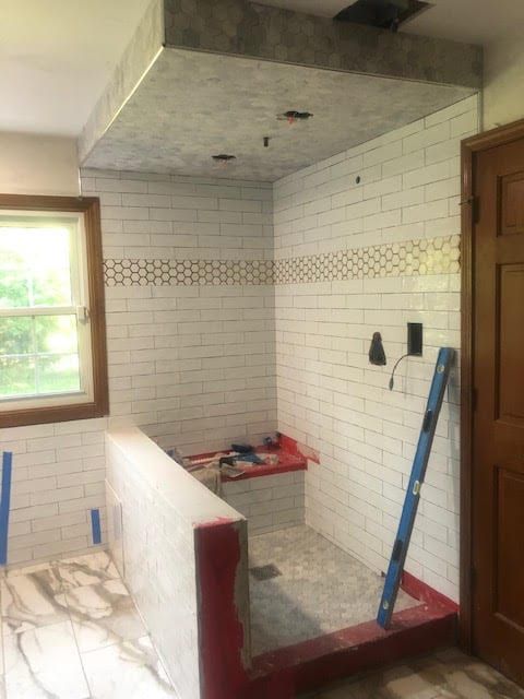 Partially tiled bathroom with a shower area, red ledge, window, and blue ladder leaning against the wall