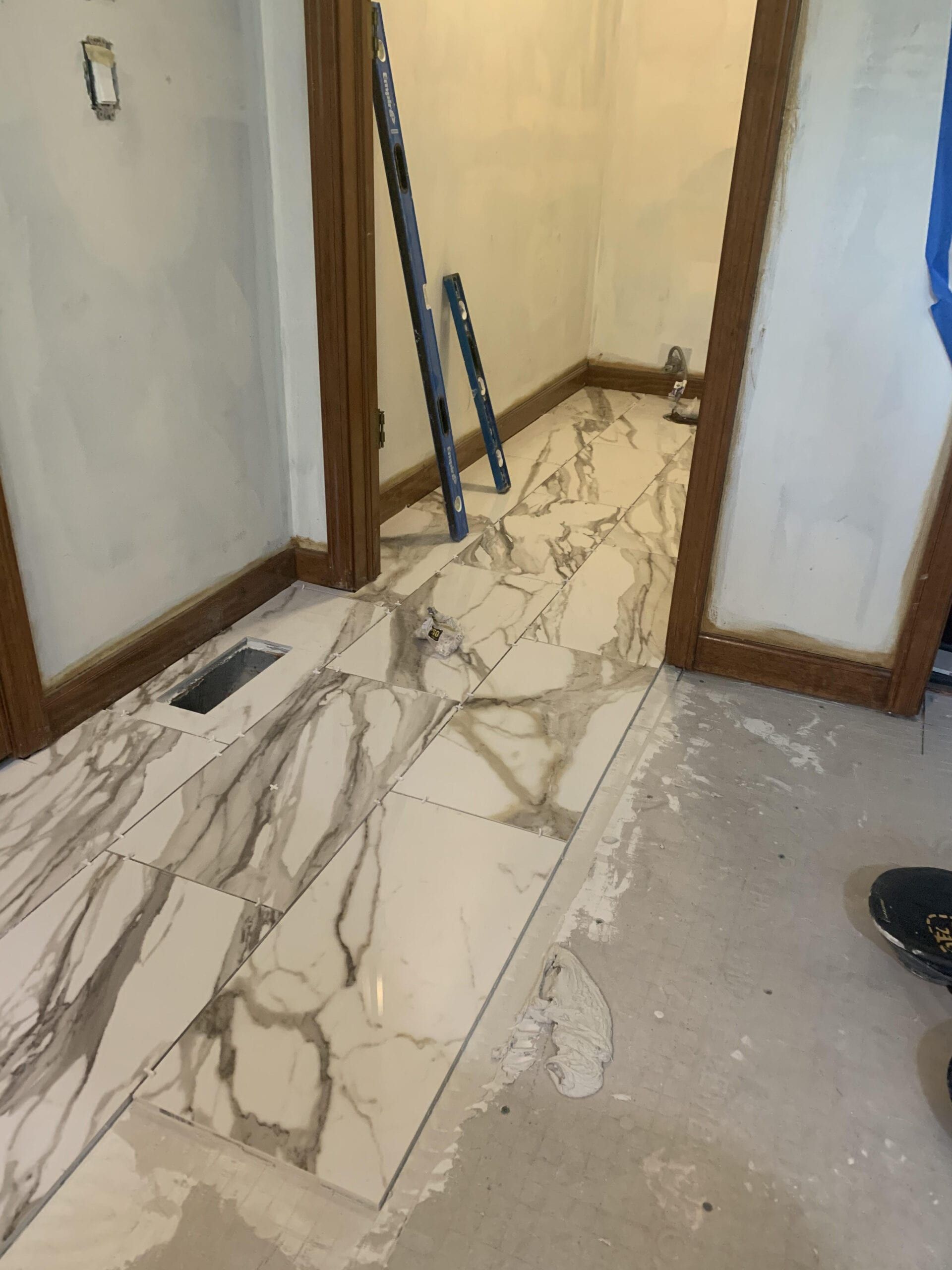 Indoor hallway with partially installed marble-pattern floor tiles and construction tools leaning against the wall