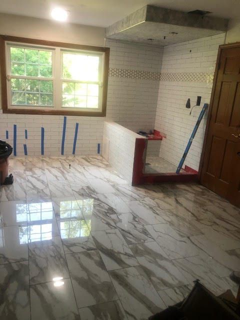 Empty tiled room with glossy white marble floor, window light, and tools leaning against the walls.