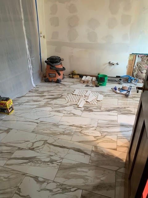Partially tiled room with marble-pattern floor, unfinished walls, and tools/materials stacked along the edges
