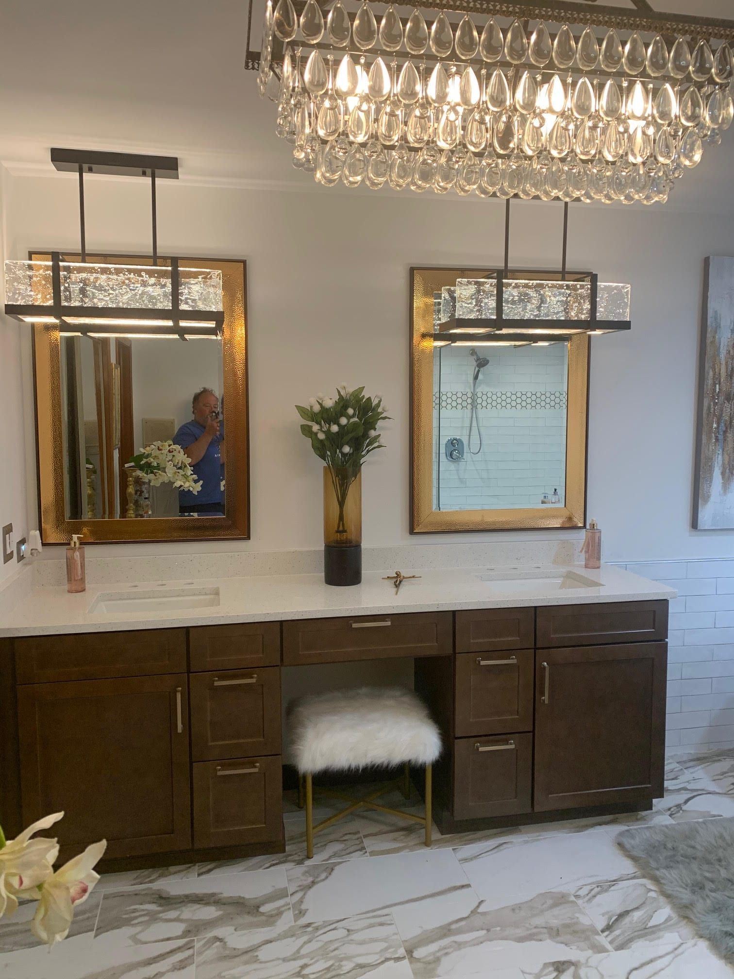 Elegant bathroom vanity with double mirrors, dark cabinets, crystal chandelier, and marble-style floor